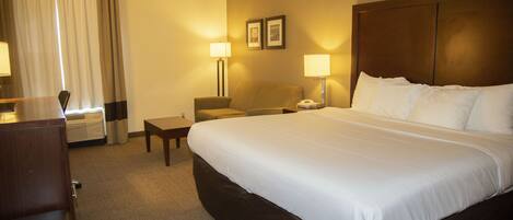 A hotel room with a large bed, a desk, a chair, and two bedside lamps.