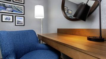 Quarto com poltrona azul, escrivaninha de madeira, espelho redondo fixado na parede e obras de arte emolduradas.