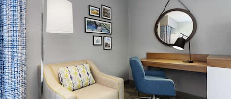 Une chambre d’hôtel équipée d’un canapé, d’un bureau, d’une chaise, d’un miroir et de tableaux encadrés accrochés au mur.