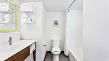 A modern bathroom with a white sink, mirror, and toilet. There are shelves with folded towels and a small framed picture on the wall.