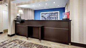 A reception desk with a blue accent wall, a lamp, and a framed picture. - Hampton Inn Amelia Island at Fernandina Beach (Fernandina Beach)