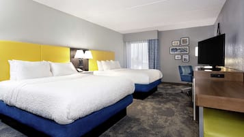 A hotel room with two beds, a desk, a chair, a TV, and framed pictures on the wall.