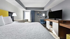 A hotel room with a large bed, a desk with a flat-screen TV, a chair, a desk lamp, and a window with curtains. - Hampton Inn Amelia Island at Fernandina Beach (Fernandina Beach)