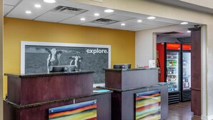 A reception desk with a 'Explore' sign, a refrigerator stocked with beverages, and a carpeted floor.