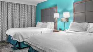 A hotel room with two beds, teal walls, and a patterned curtain.