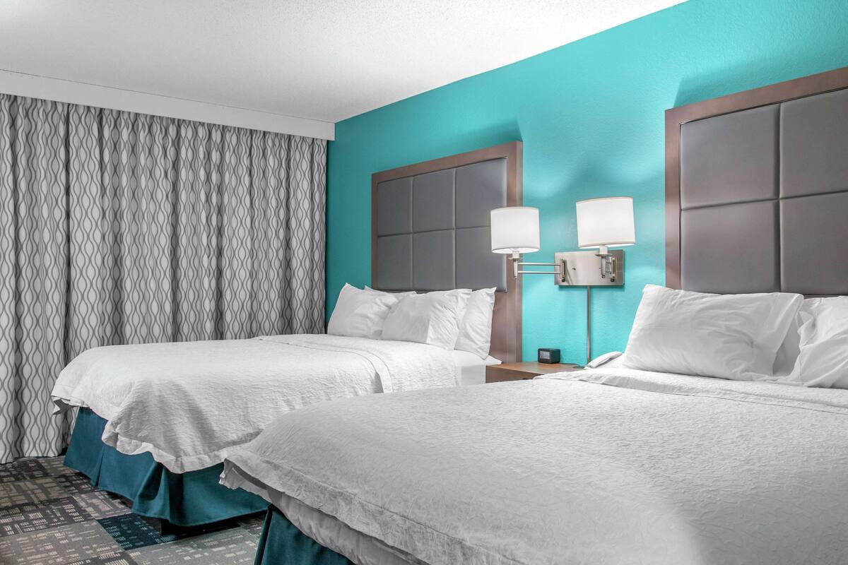Habitació d'hotel amb dos llits, parets color turquesa i cortina amb dibuixos.