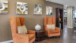 A lobby with two orange armchairs, a small round table, and three wall-mounted mirrors.