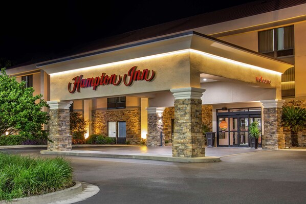 A Hampton Inn hotel entrance with stone pillars, a well-lit facade, and a welcoming sign.