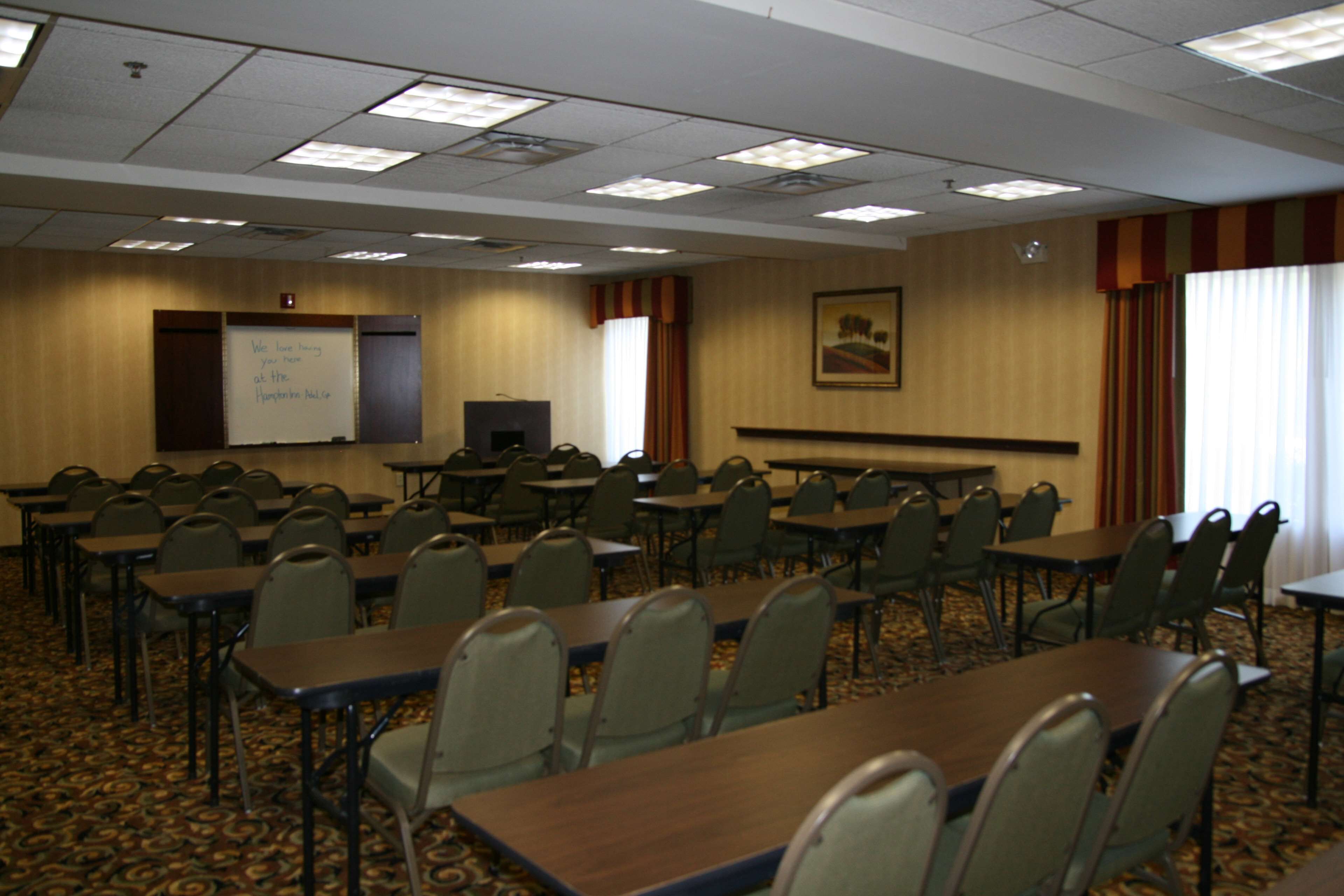 A conference room with multiple tables and chairs, a whiteboard, and a painting on the wall.