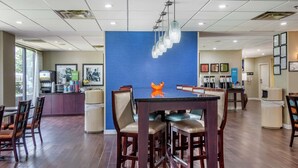 A modern hotel lobby with a blue accent wall, a bar area, and a seating area with wooden chairs and tables.