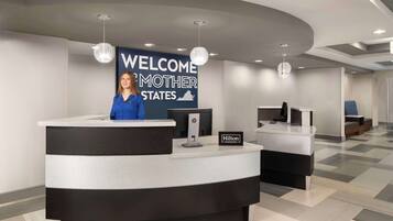 Een hotel receptie met een gebogen balie, een groot welkomstbord en een receptioniste.