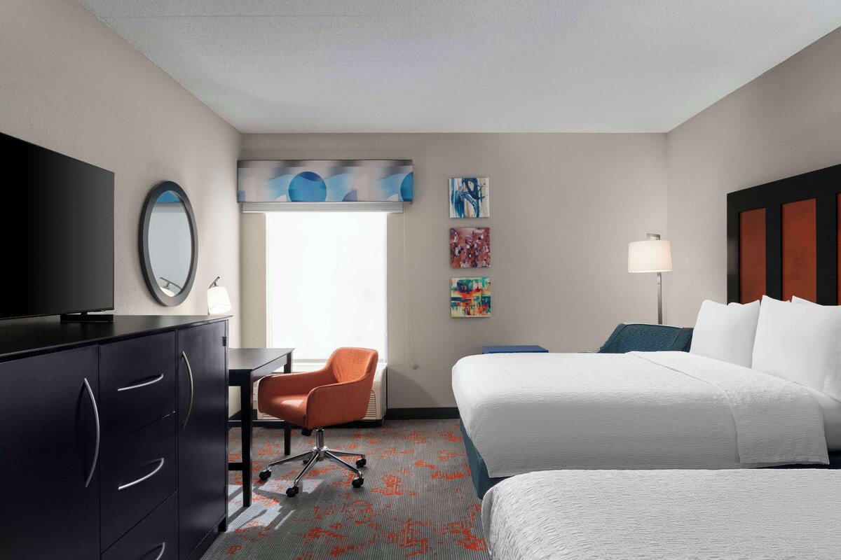 Een hotelkamer met een bed, een bureau, een stoel, een televisie en kunstwerken aan de wanden.