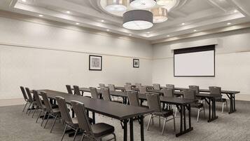 A conference room with multiple tables and chairs, a projector screen, and framed artwork on the wall.