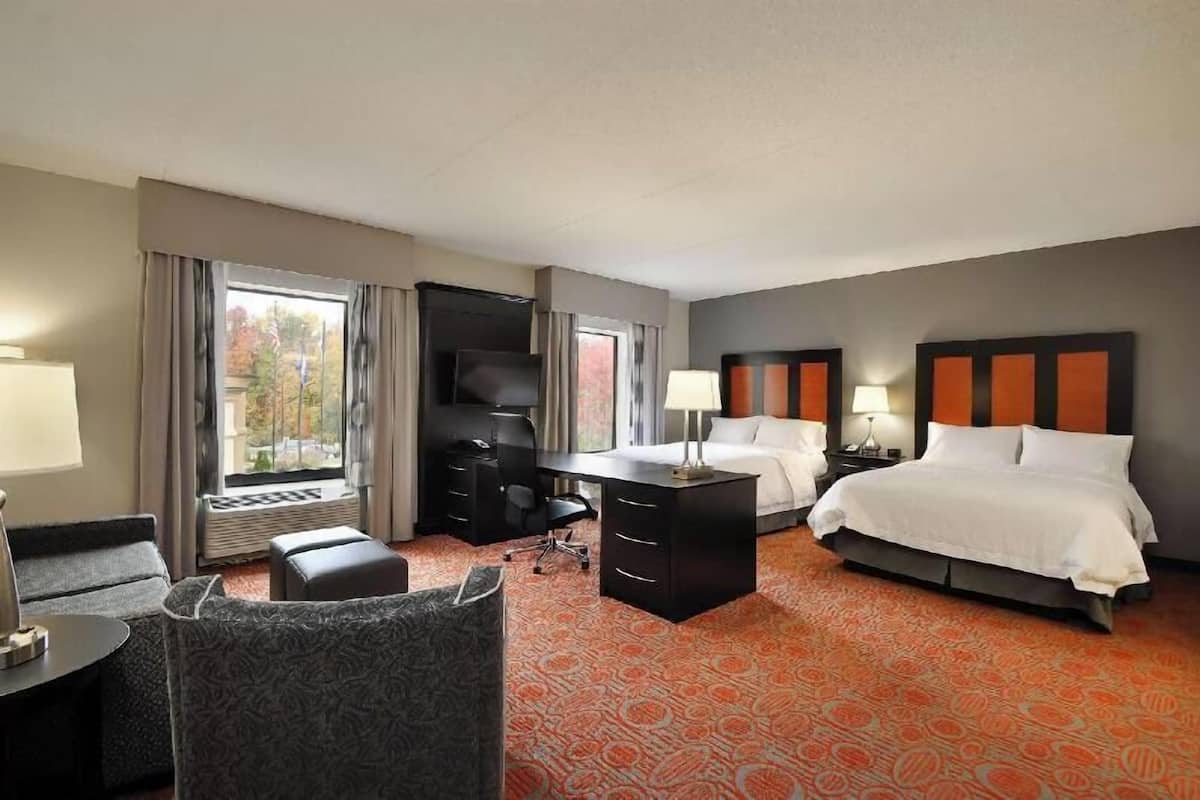 A hotel room with a bed, desk, chair, and a large window.