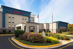 A Hampton Inn hotel with a clear blue sky, American flags, and well-maintained landscaping.