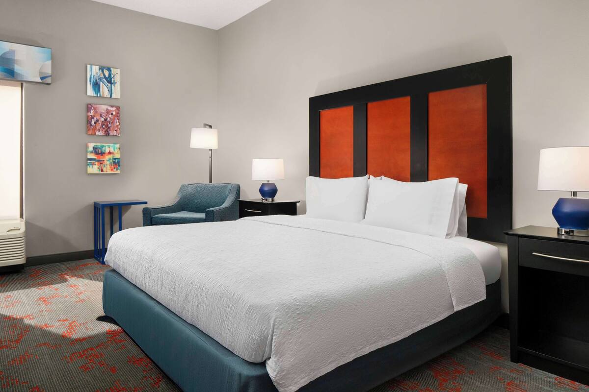 A hotel room with a large bed, a chair, a desk, and a lamp.