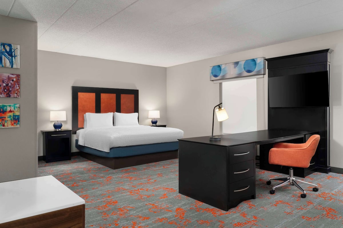 A hotel room with a bed, desk, chair, and a TV on a stand.