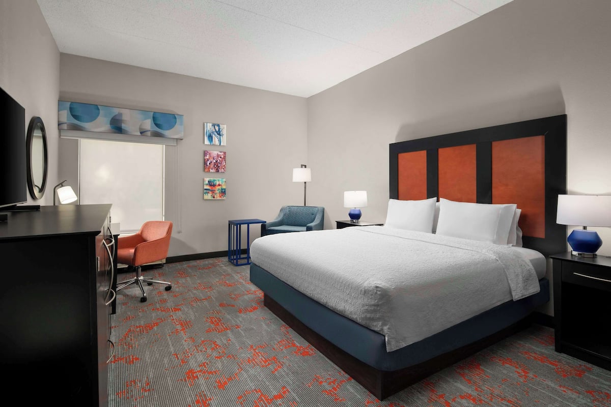 A hotel room with a large bed, a desk, a chair, and a TV.