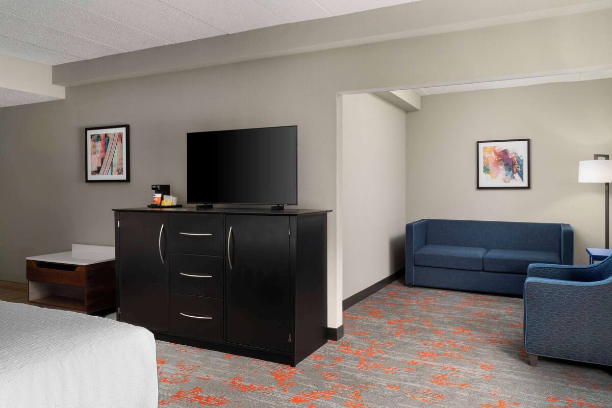 A hotel room with a bed, a dark wooden cabinet with a flat-screen TV, a blue sofa, and a small table.