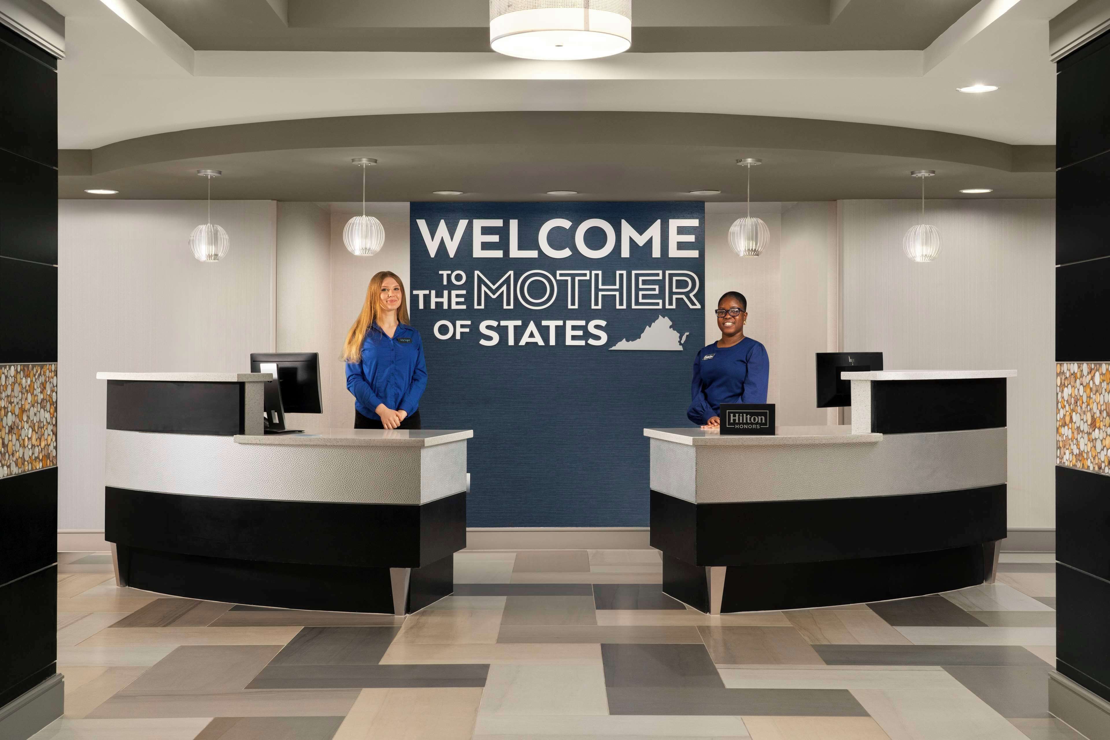 A reception area with a "Welcome to the Mother of States" banner, two receptionists, and a modern design with black and white furniture.
