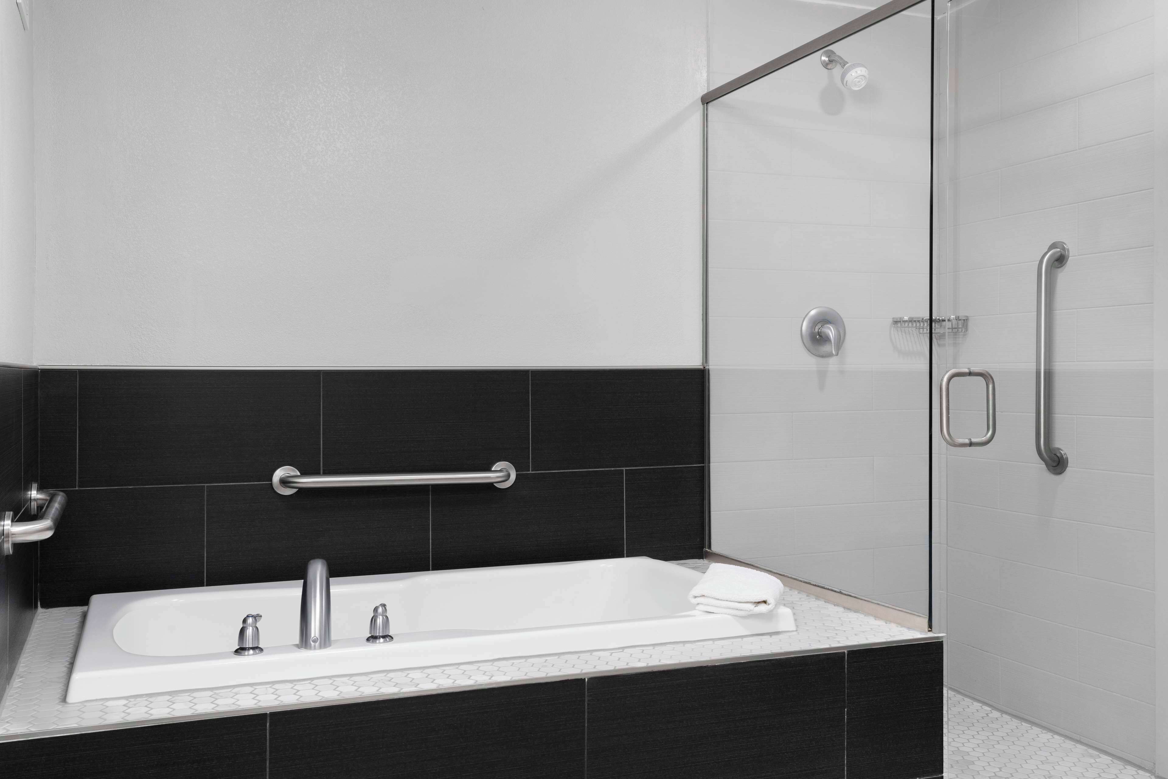 Een moderne badkamer met een badkuip, een glazen douchecabine en een handgreep.