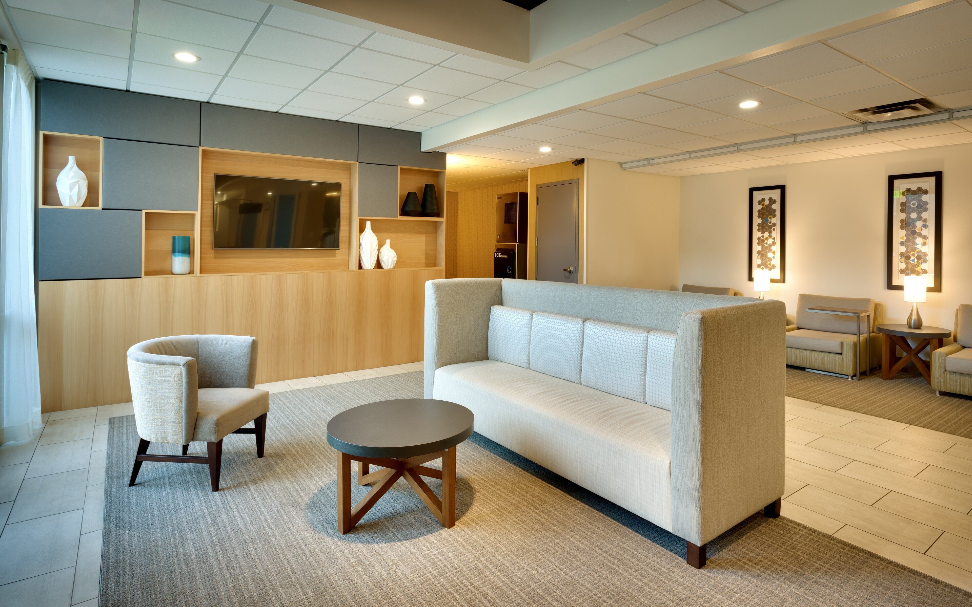 A modern hotel lobby with a sofa, chairs, a small table, and decorative wall art.
