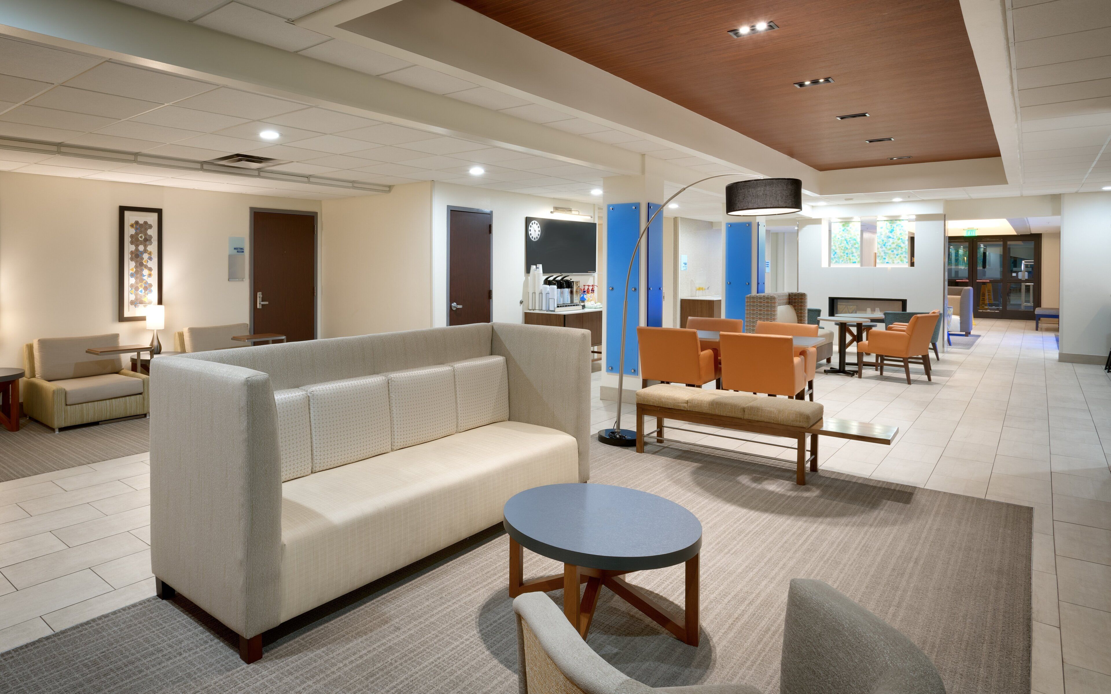 A modern hotel lobby with a sofa, chairs, a round table, and a flat-screen TV.