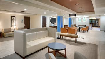A modern hotel lobby with a sofa, chairs, a round table, and a flat-screen TV.
