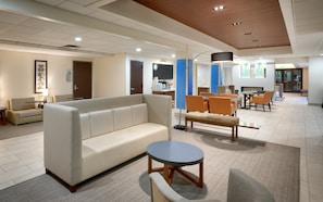 Un hall d’hôtel moderne avec un canapé, des fauteuils, une table ronde et un téléviseur à écran plat.