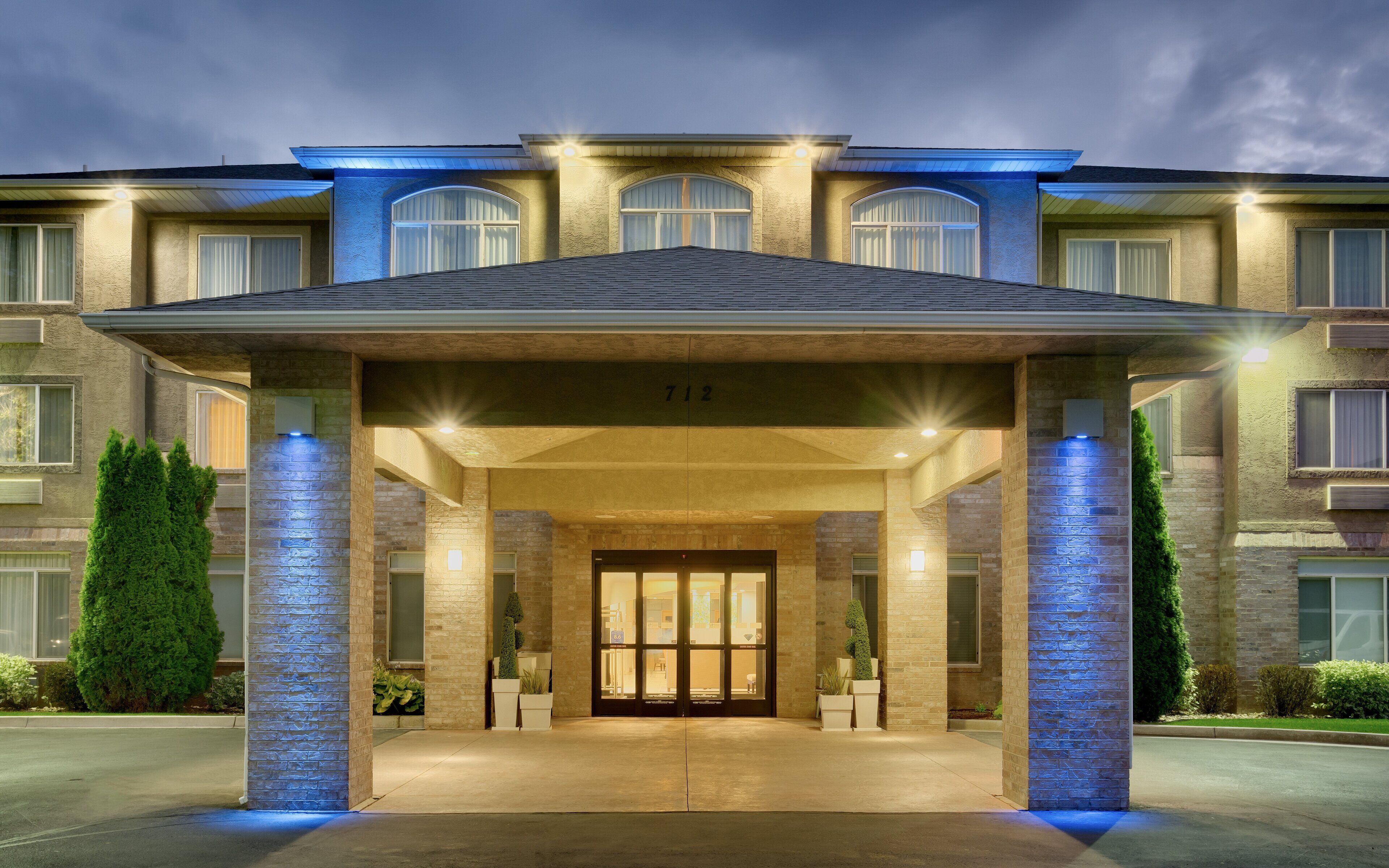 A hotel entrance with a covered walkway, large windows, and a number '712' above the doors.