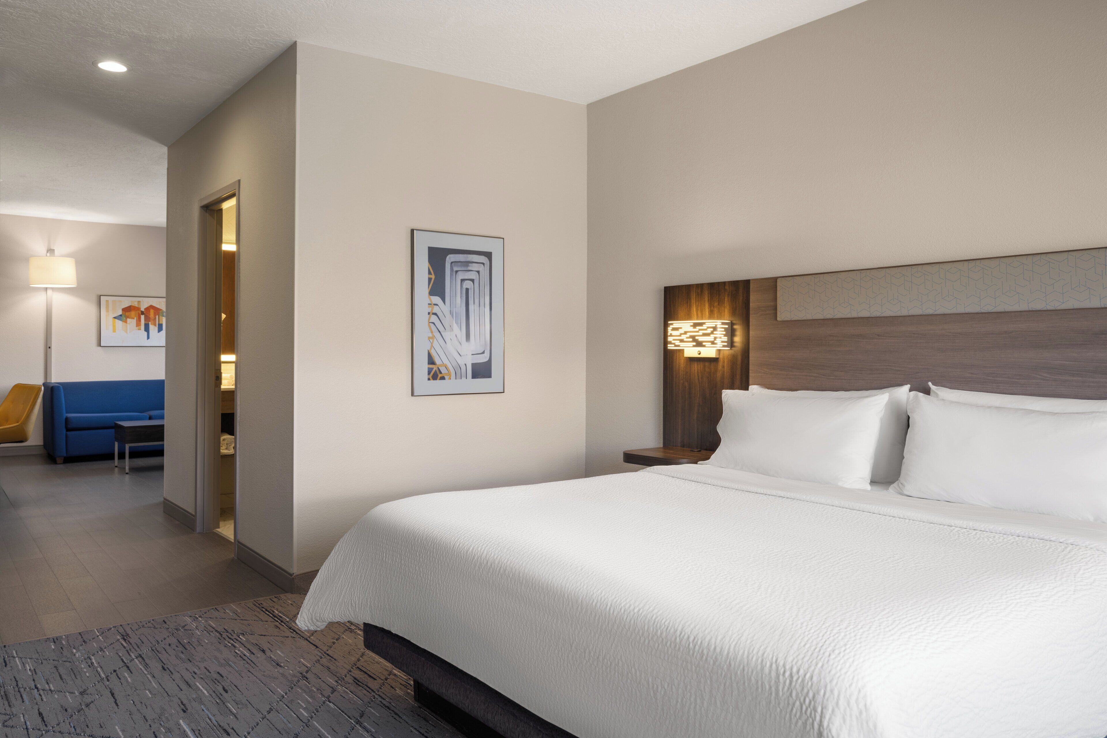 Une chambre d’hôtel avec un grand lit, une table de chevet avec une lampe, un canapé bleu et un tableau au mur.