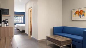 A modern hotel room with a blue sofa, a wooden coffee table, a TV, and a bed with white bedding.