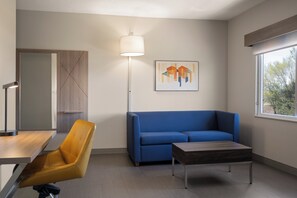A modern living room with a blue sofa, a wooden coffee table, a yellow chair, a floor lamp, and a framed abstract artwork on the wall. - Holiday Inn Express & Suites American Fork - North Provo by IHG (American Fork)