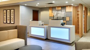 A hotel reception area with a sofa, two reception desks, and framed artwork on the wall.