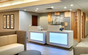 A hotel reception area with a sofa, two reception desks, and framed artwork on the wall. - Holiday Inn Express & Suites American Fork - North Provo by IHG (American Fork)