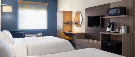 A hotel room with two beds, a desk, a chair, a TV, a coffee maker, and a refrigerator.