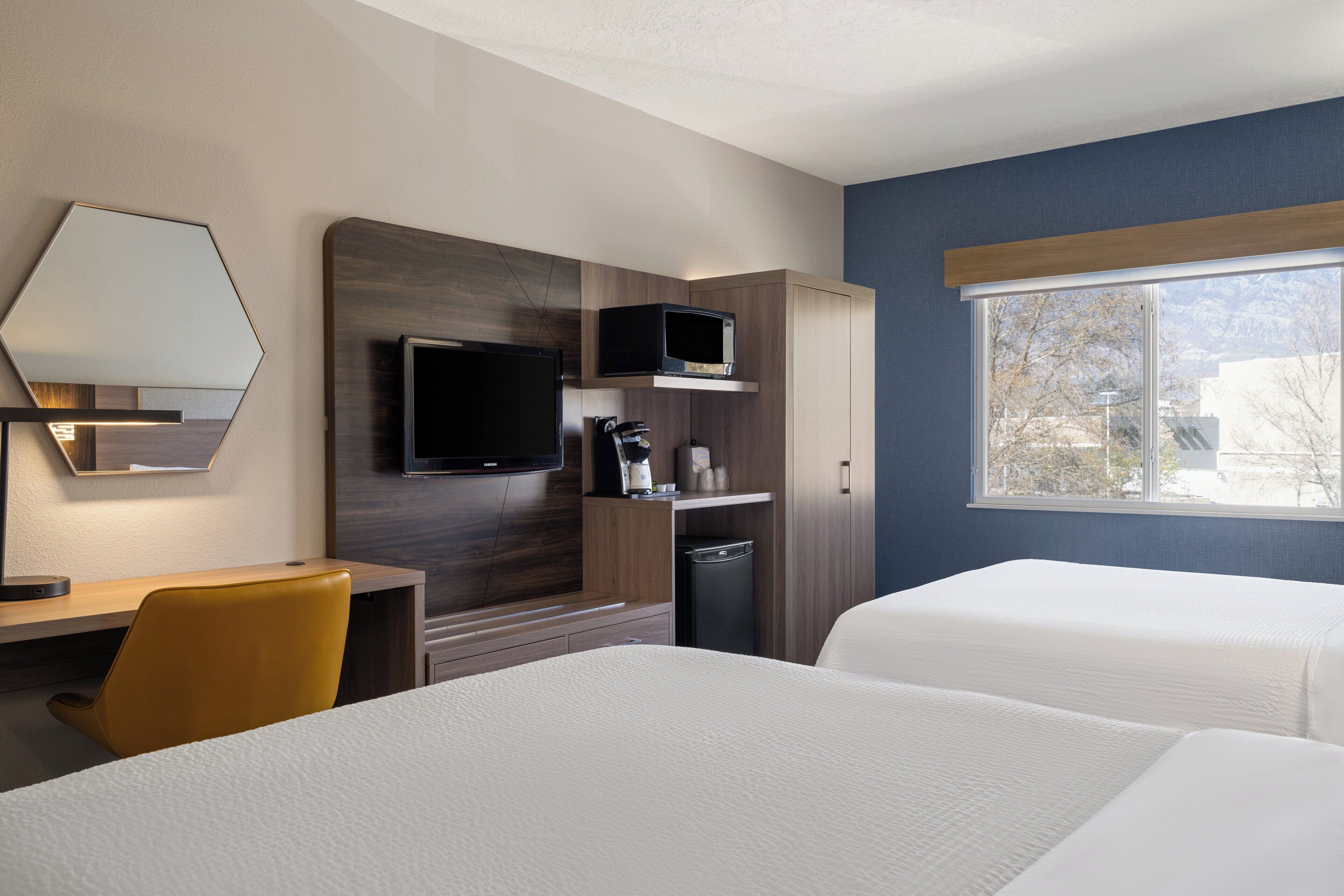 A hotel room with a bed, a desk, a chair, a TV, and a window with a view.