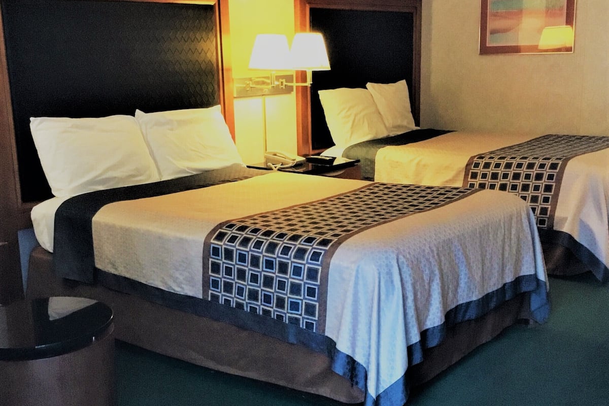 Una habitación de hotel con dos camas, una mesita de noche, una lámpara y un cuadro en la pared.