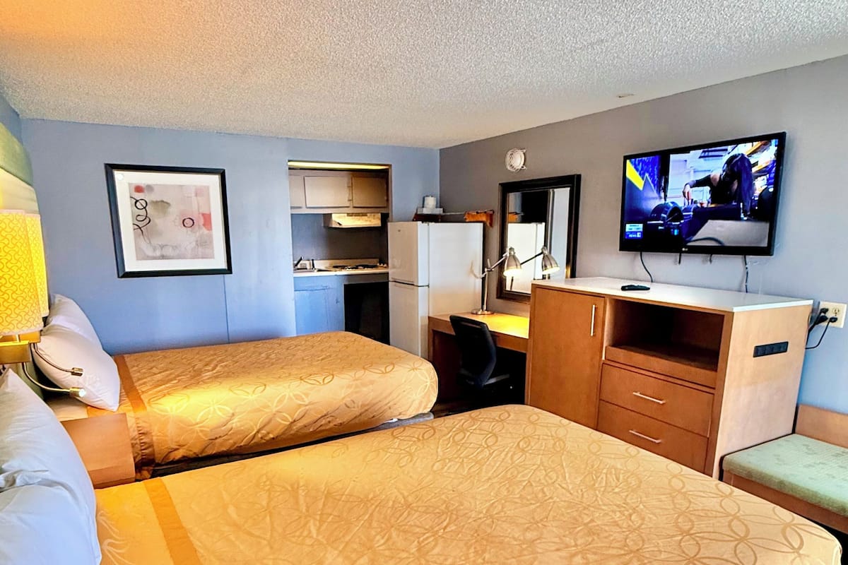 Habitación de hotel con dos camas, un escritorio, televisión y kitchenette.
