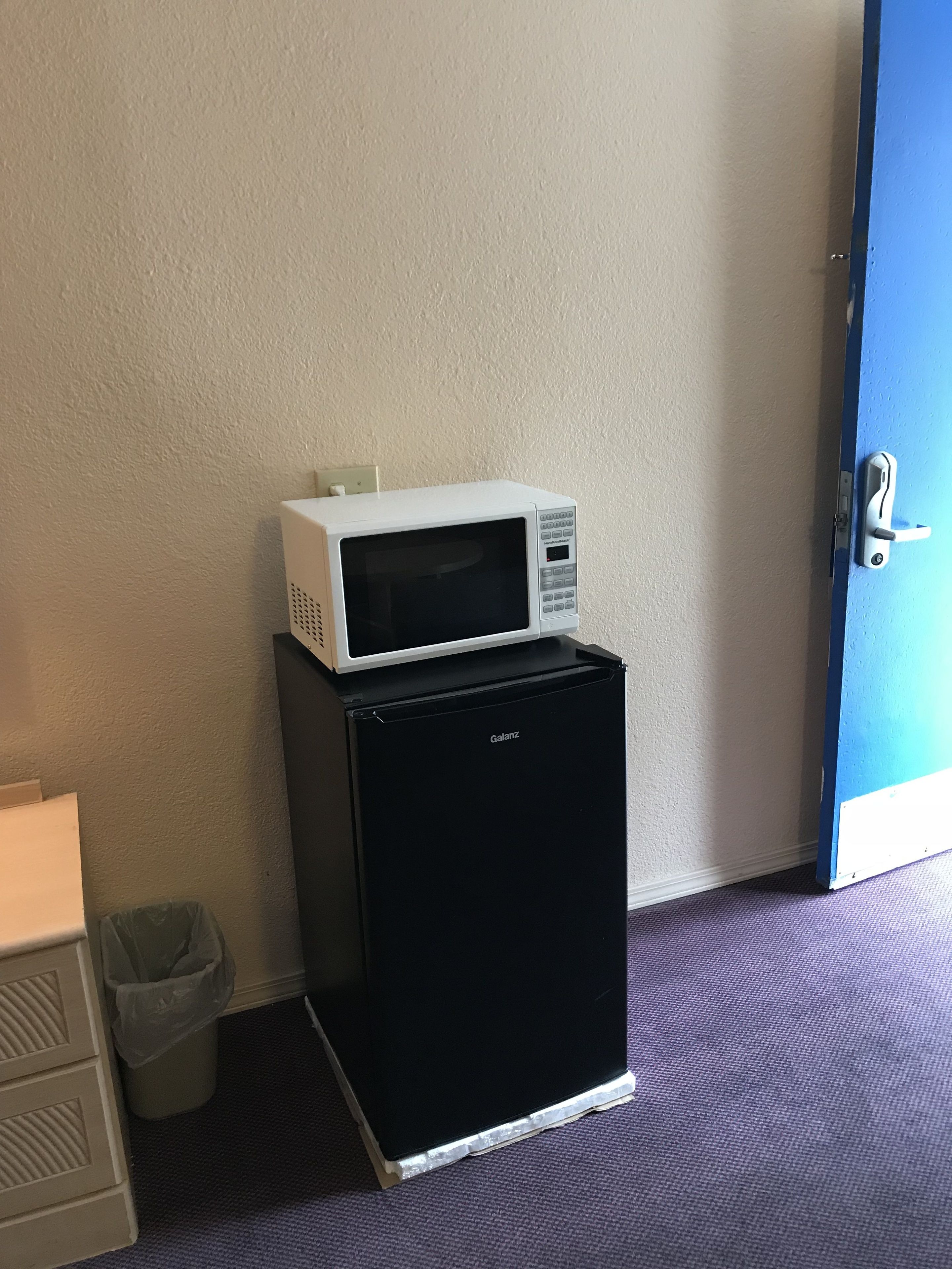 Un frigorífic petit amb un microones a la part superior, col·locat al costat d'una paret i una porta a prop.