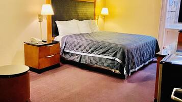 Una habitación de hotel con cama, lámparas de noche, mesita de noche, una mesa redonda y cómoda.