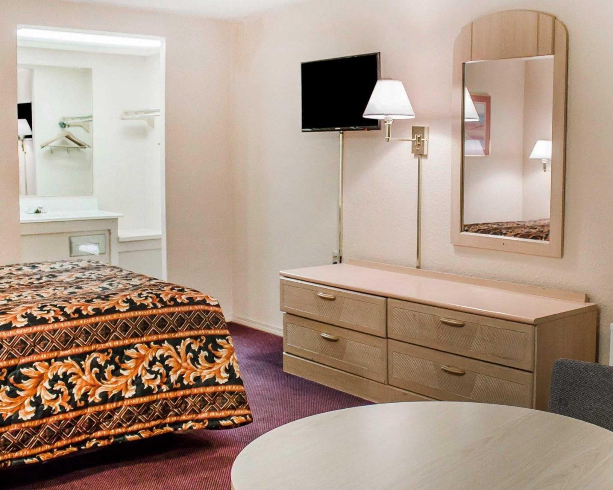 A hotel room with a bed, a dresser, a television, a mirror, and a table.