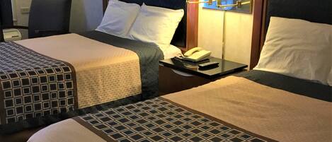 A hotel room with two beds, a chair, a nightstand with a lamp, and a phone.