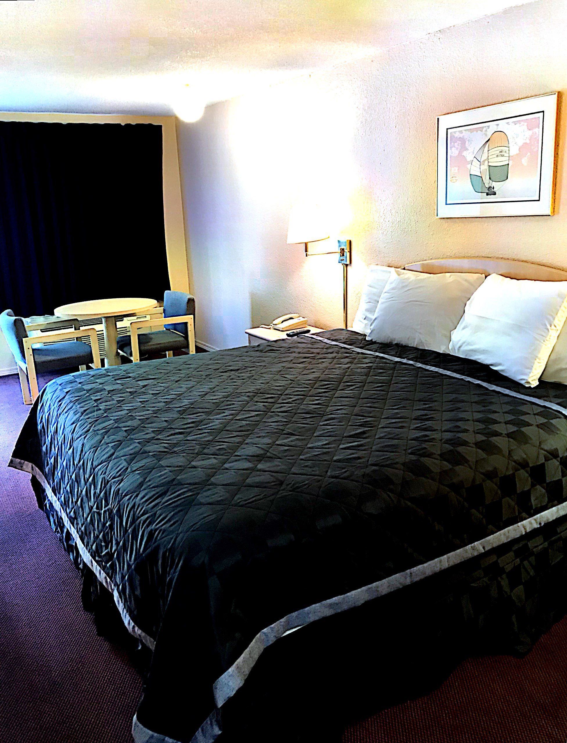 Ein Hotelzimmer mit einem großen Bett, einem Schreibtisch mit Stuhl, einer Lampe und einem Bild an der Wand.