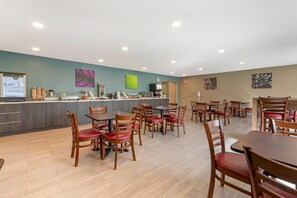 A modern restaurant with wooden tables and chairs, a counter with coffee machines, and artwork on the walls.