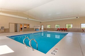 An indoor swimming pool with clear lane markings, a lifeguard chair, and a poolside area with chairs.