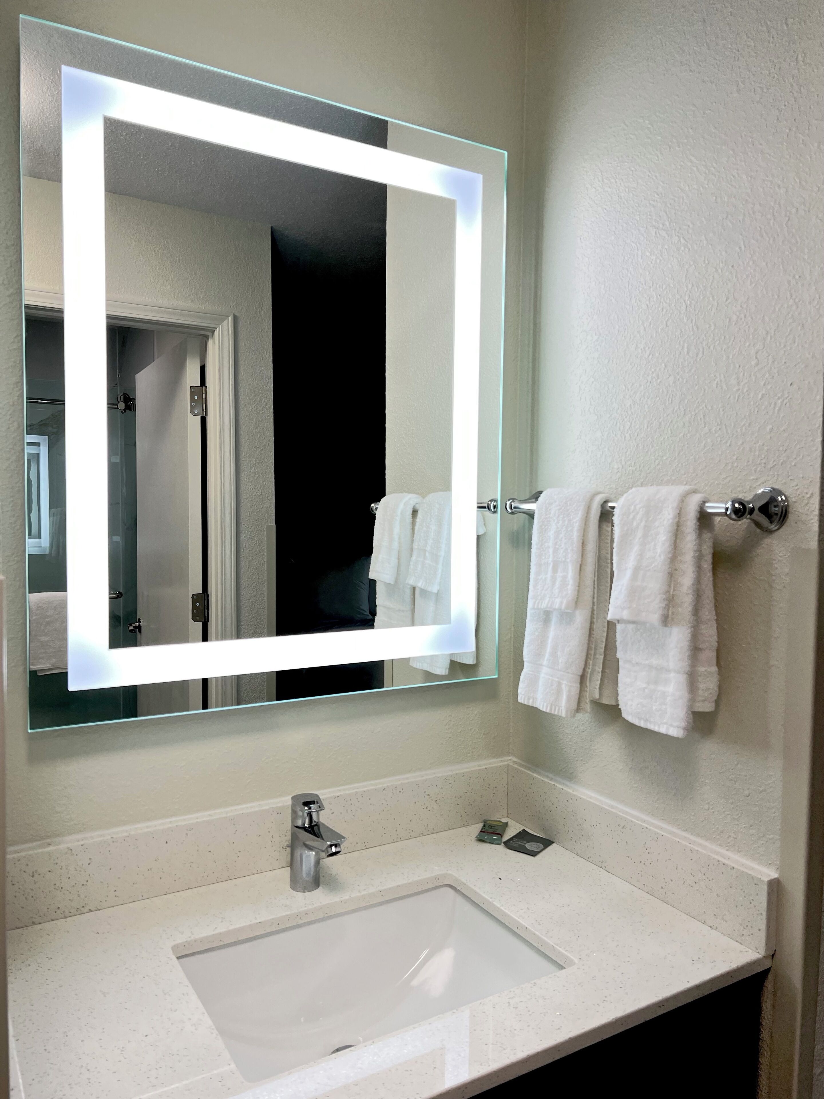 A bathroom with a large mirror, a white sink, and two towels hanging on a rack.
