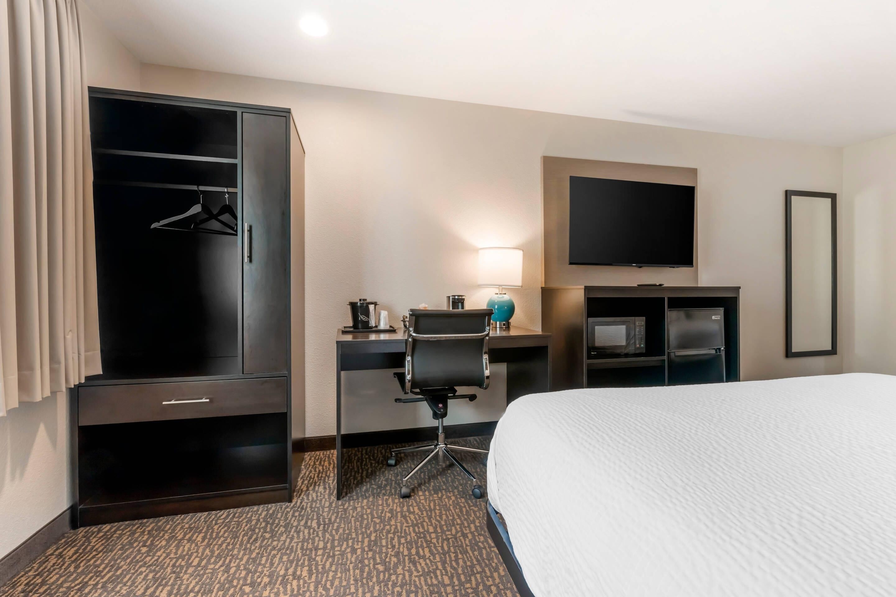 A hotel room with a large bed, a desk with a chair, a wardrobe, a flat-screen TV, and a minibar.