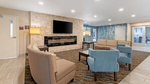 A modern living room with a stone wall, a flat-screen TV, beige sofas, and a patterned rug.