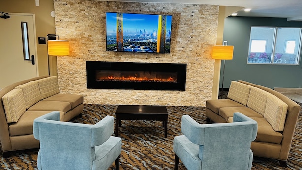 A lobby with a stone wall, a flat-screen TV, a fireplace, two sofas, and two lamps.